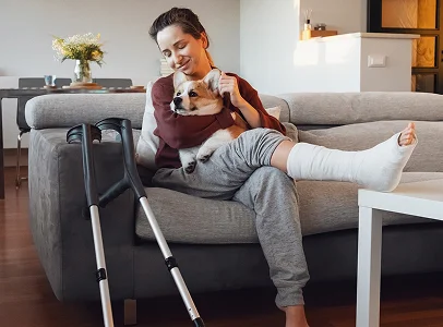 Femme souriante avec une jambe cassée et des béquilles, câlinant un corgi à l'extérieur à Paris 17eme arrondissement en Ile-de-France 75